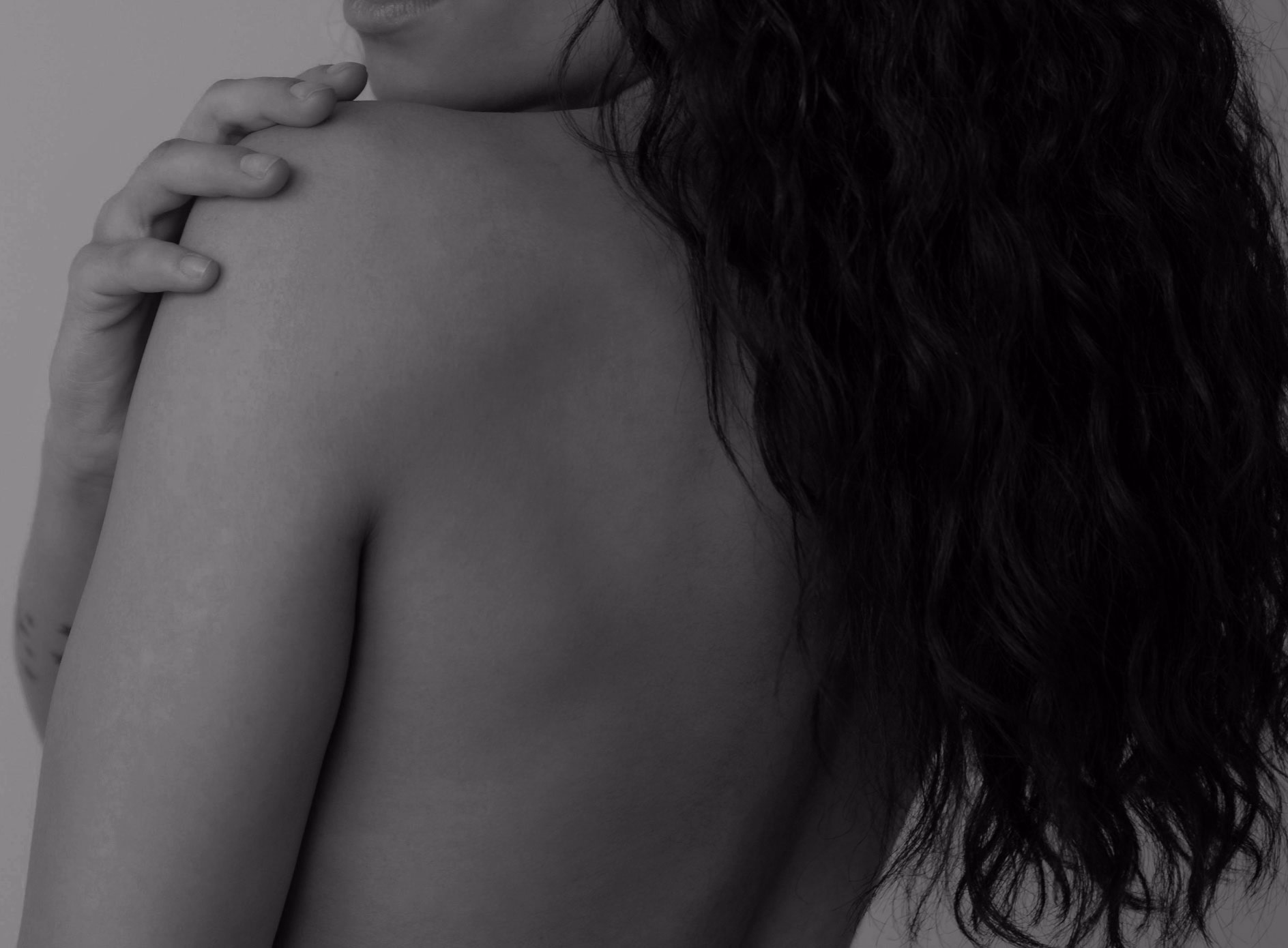 Close-up of a woman's back with a hand resting on her shoulder