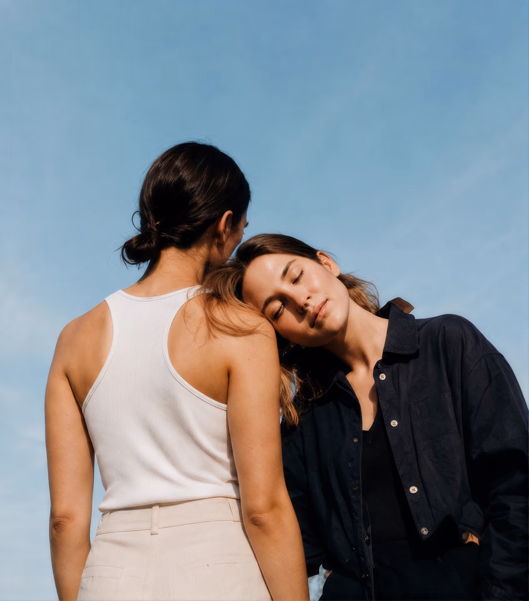 Two women leaning close together under a blue sky