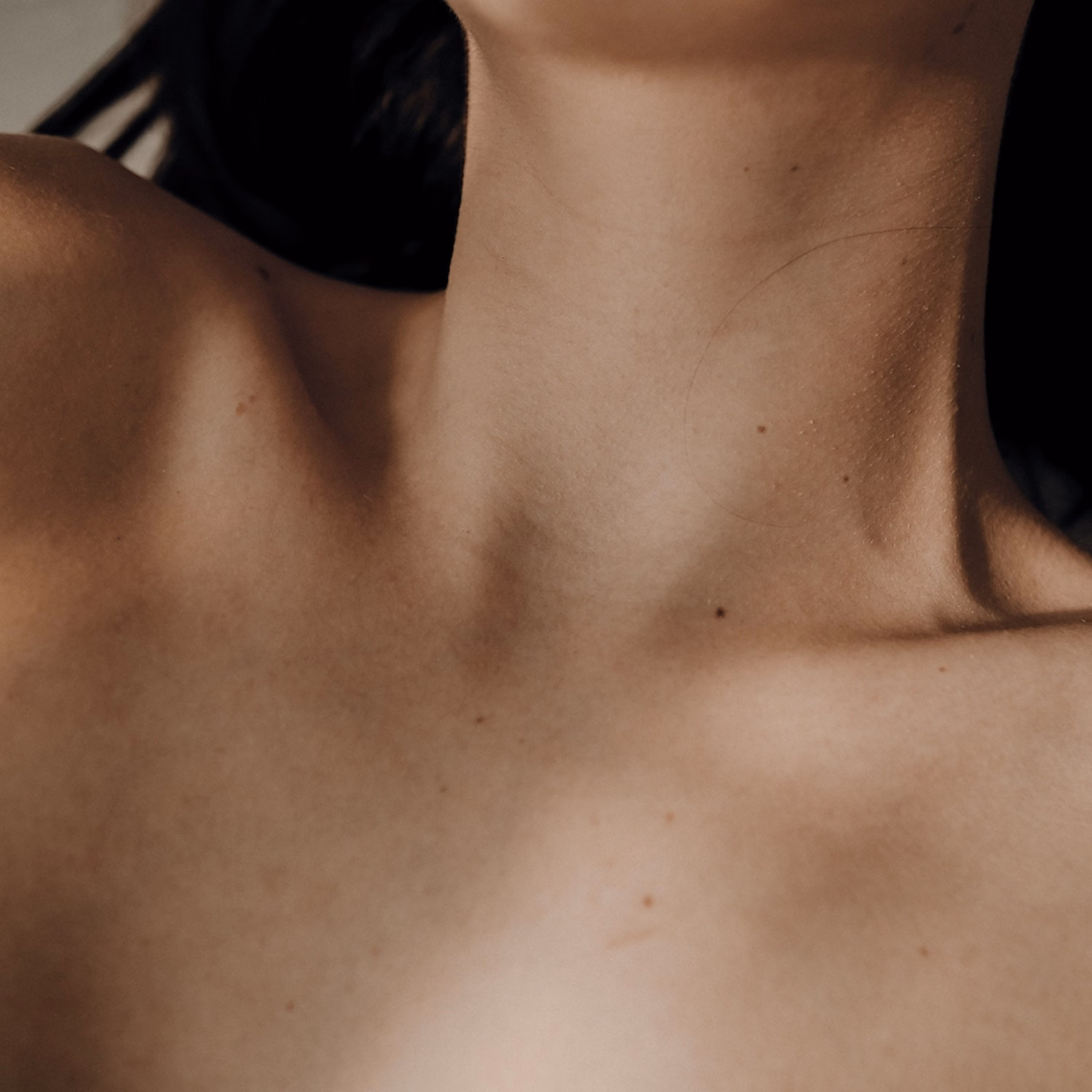 Close-up of a woman's neck and collarbone in soft, warm light